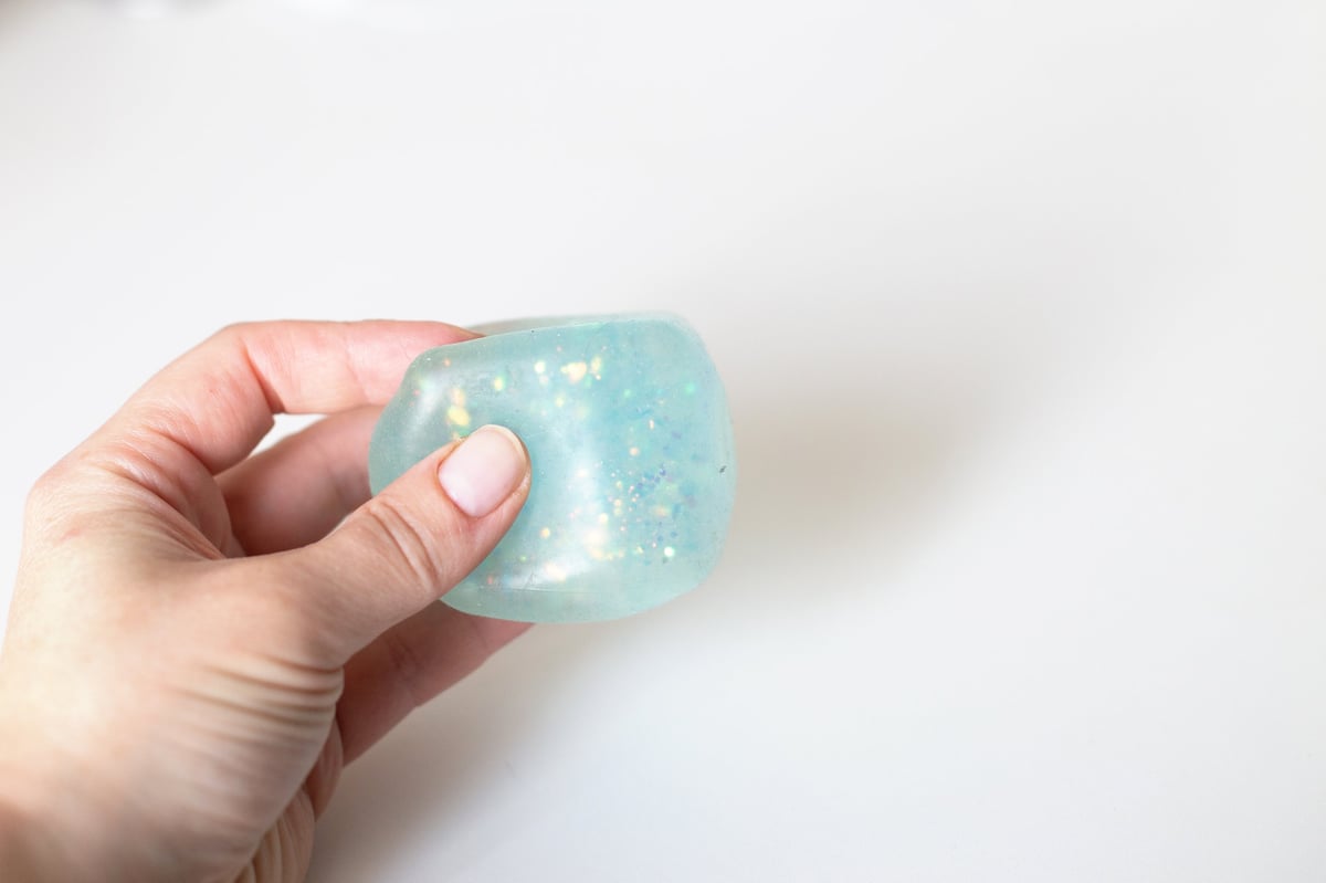 A hand deforming a light blue glitter squishy toy